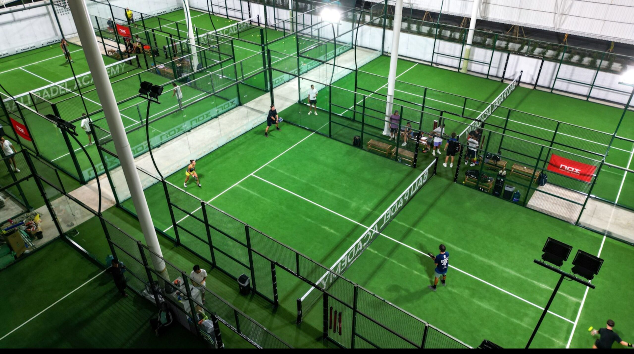 Aerial view of indoor padel courts at Bali Padel Academy in Canggu with green artificial turf, glass walls and professional lighting