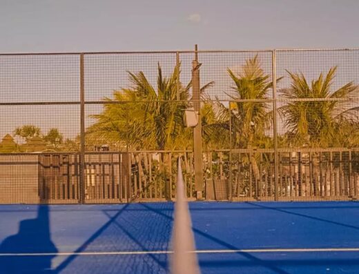Outdoor blue padel court at Holywings Padel Club, Atlas Beach Club Bali, with palm trees and golden-hour light