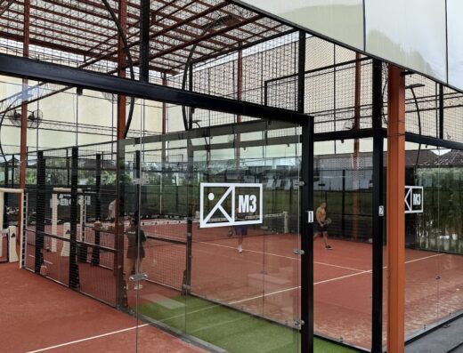 Glass-walled padel courts in play at Jungle Padel Kedungu