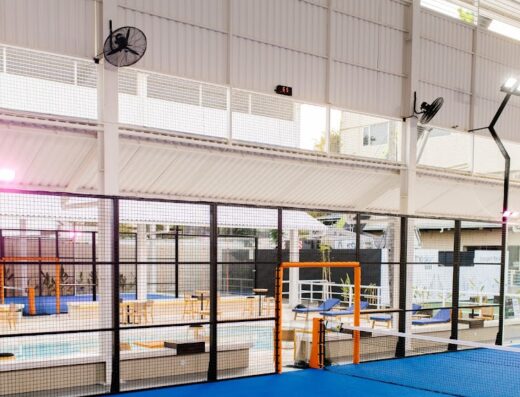 Indoor padel court with fans and poolside seating at Liga.Tennis Padel Seminyak