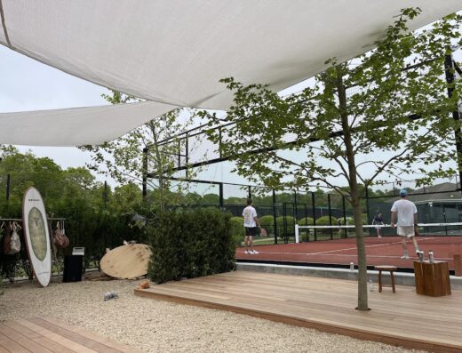 Shaded lounge deck beside outdoor padel and clay courts at Brisas East Hampton